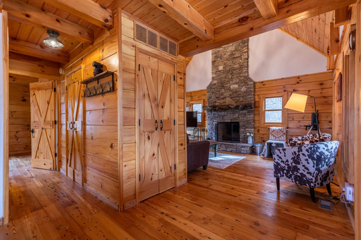This image highlights a rustic stone fireplace surrounded by wooden beams, a cowhide chair, and barn doors, creating a warm and communal ambiance. The room suggests group gatherings and features an inviting setting for evening relaxation or entertainment.