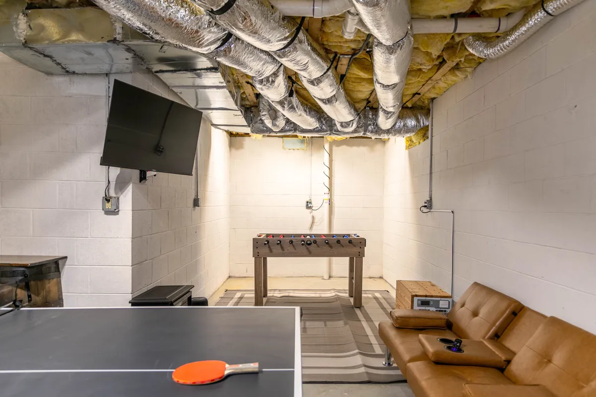 An energetic interior game room featuring a ping pong table, foosball table, couch, and TV, designed for lively social gatherings. The space is both fun and inviting, offering a perfect spot to regroup and unwind after a day filled with mountain adventures.