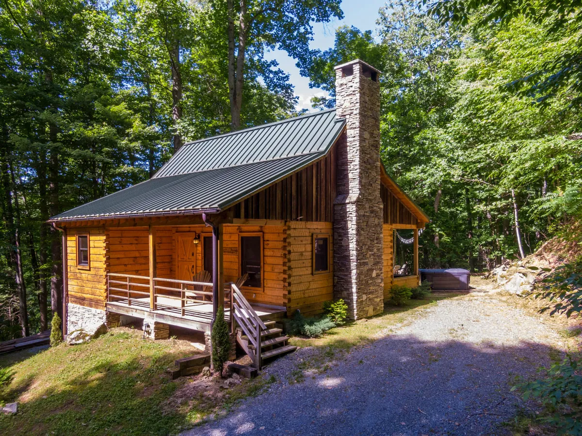 The hero image showcases a charming wooden cabin nestled among towering trees, with a striking stone chimney and a spacious deck perfect for relaxing. The tranquil forest setting hints at opportunities for nature walks or enjoying peaceful mornings with coffee on the porch.