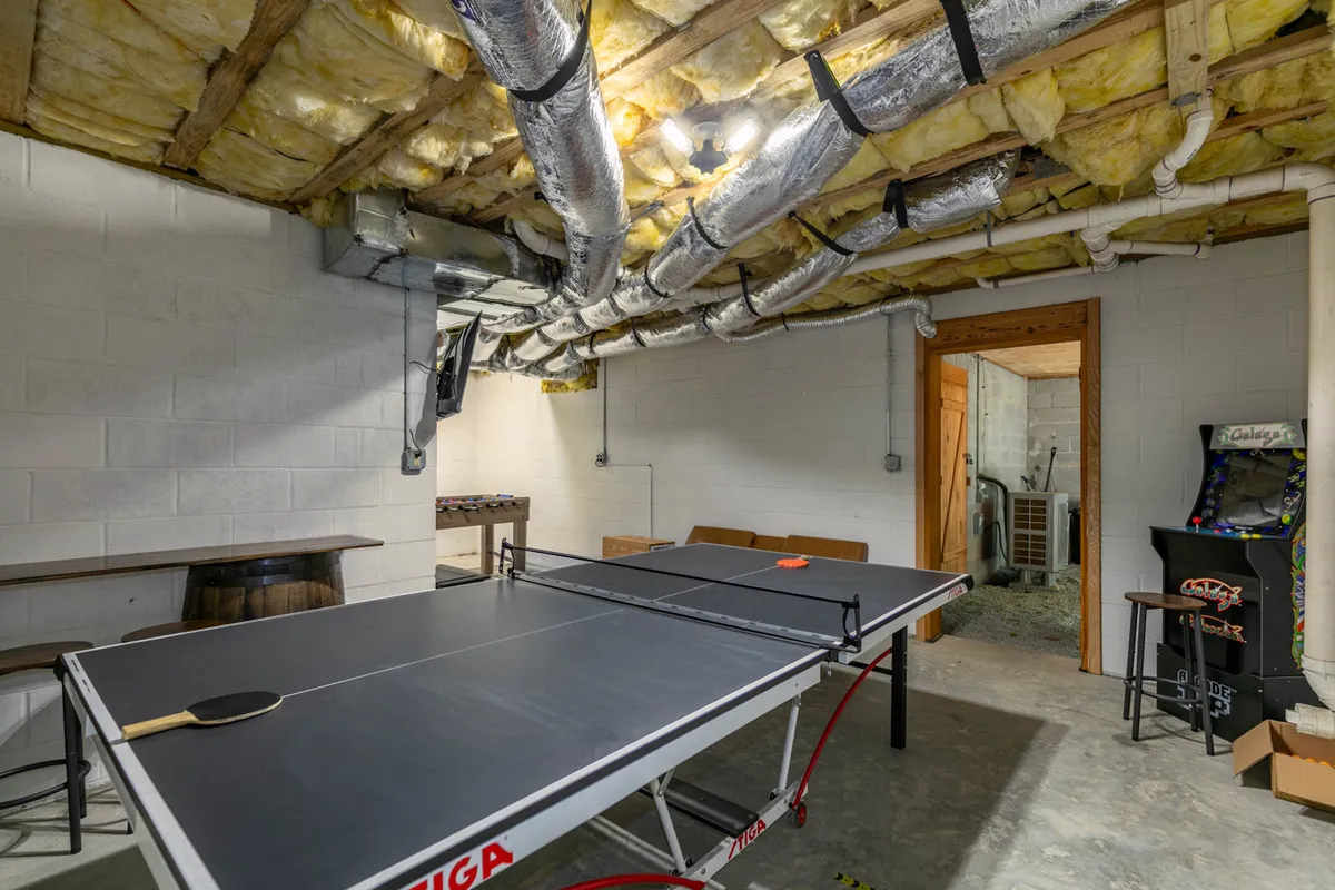 The game room’s ping pong table takes center stage, accompanied by barrel-style seating and an arcade machine on one side. The room’s playful ambiance is underscored by the presence of multiple game options and seating for socializing.