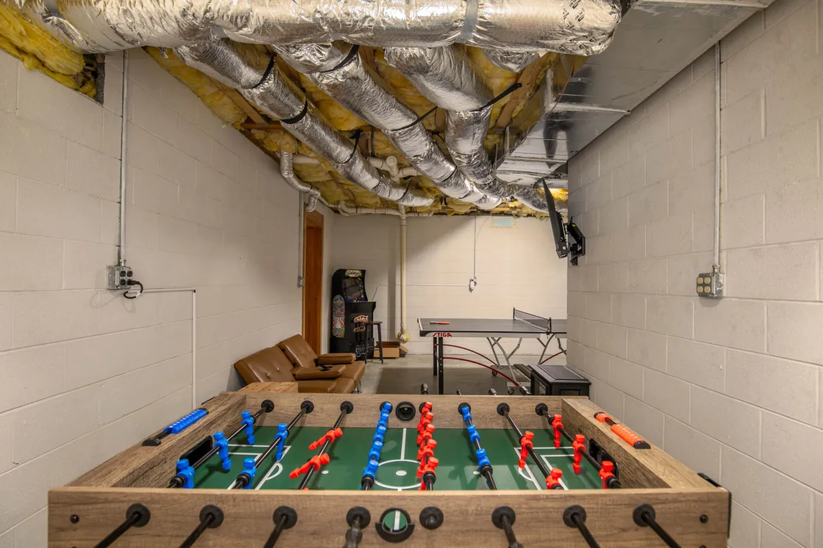 Inside a lively game room, this image displays a foosball table, ping pong table, and leather chairs, suggesting a space designed for fun, friendly competition, and shared laughter among family members.