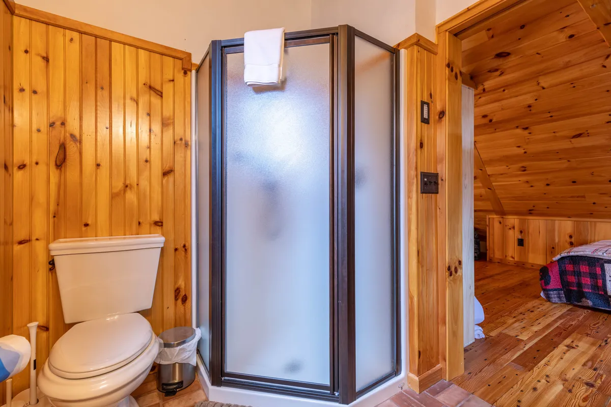 A bright and clean bathroom with a shower stall, wooden walls, a toilet, and neatly hung towels. The space feels refreshing and inviting, ideal for personal relaxation and self-care.