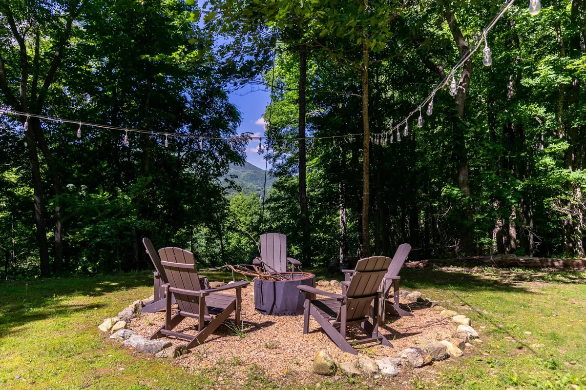 A cozy fire pit area set with Adirondack chairs under glowing string lights, nestled in a peaceful outdoor setting. The space beckons for evening gatherings, storytelling, and stargazing under the clear mountain sky.